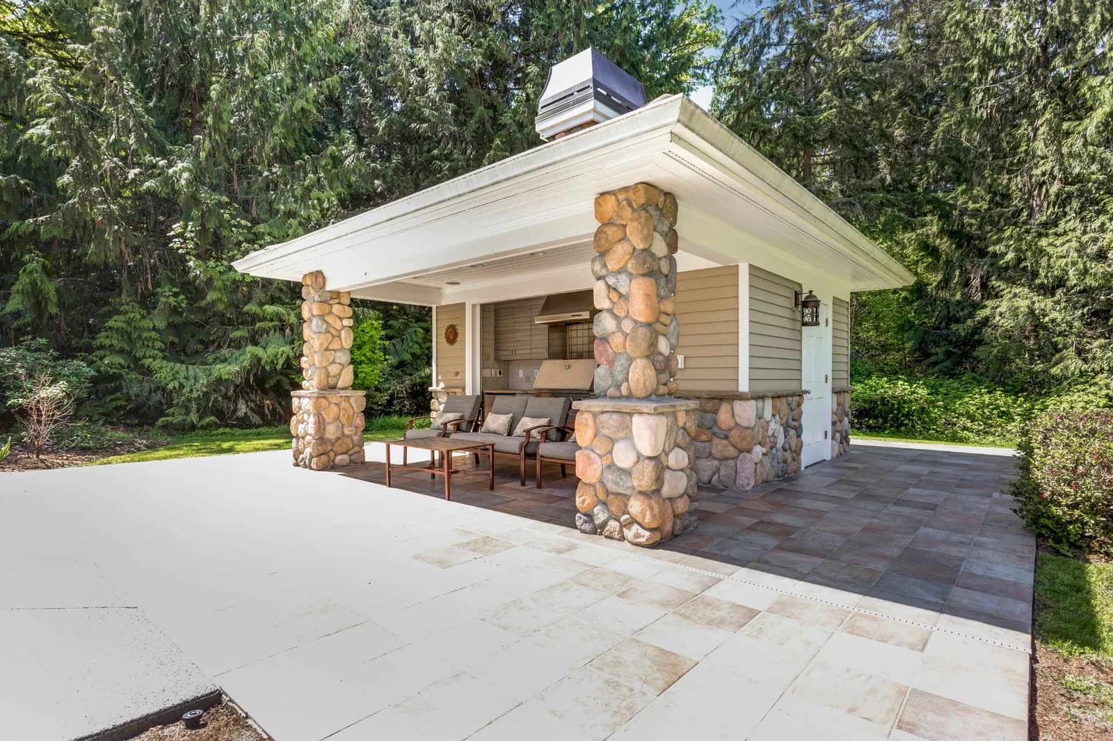 Outdoor kitchen with stove, hood, sink and dining area under pergola