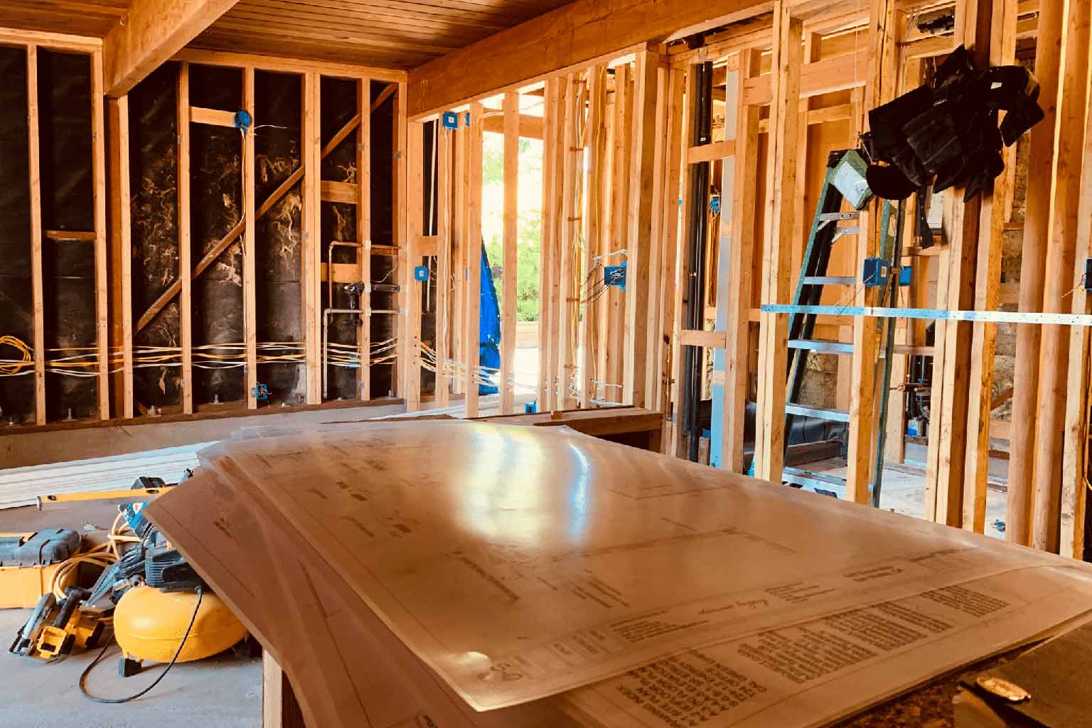 ADU interior under construction with exposed wood framing, electrical wiring, and blueprints