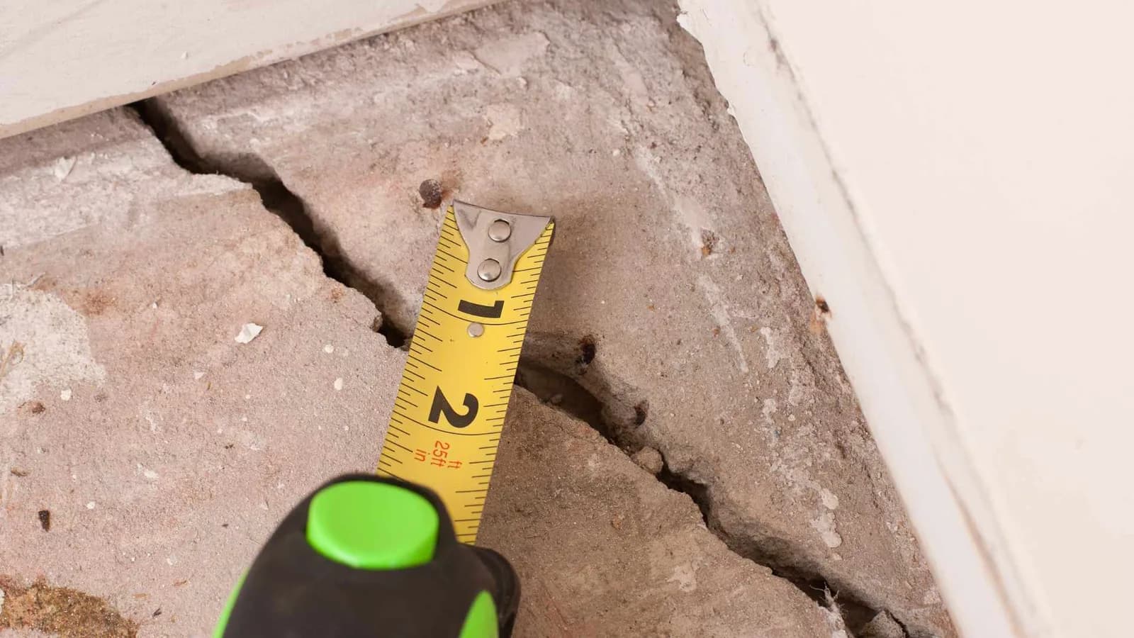 cracks in slab foundation with a measuring tape showing the size of the crack
